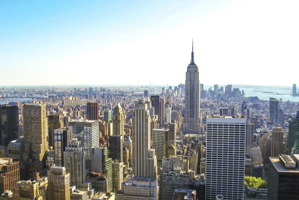 Aerial view of New York City with skyscrapers and the Empire State Building under a bright sky.