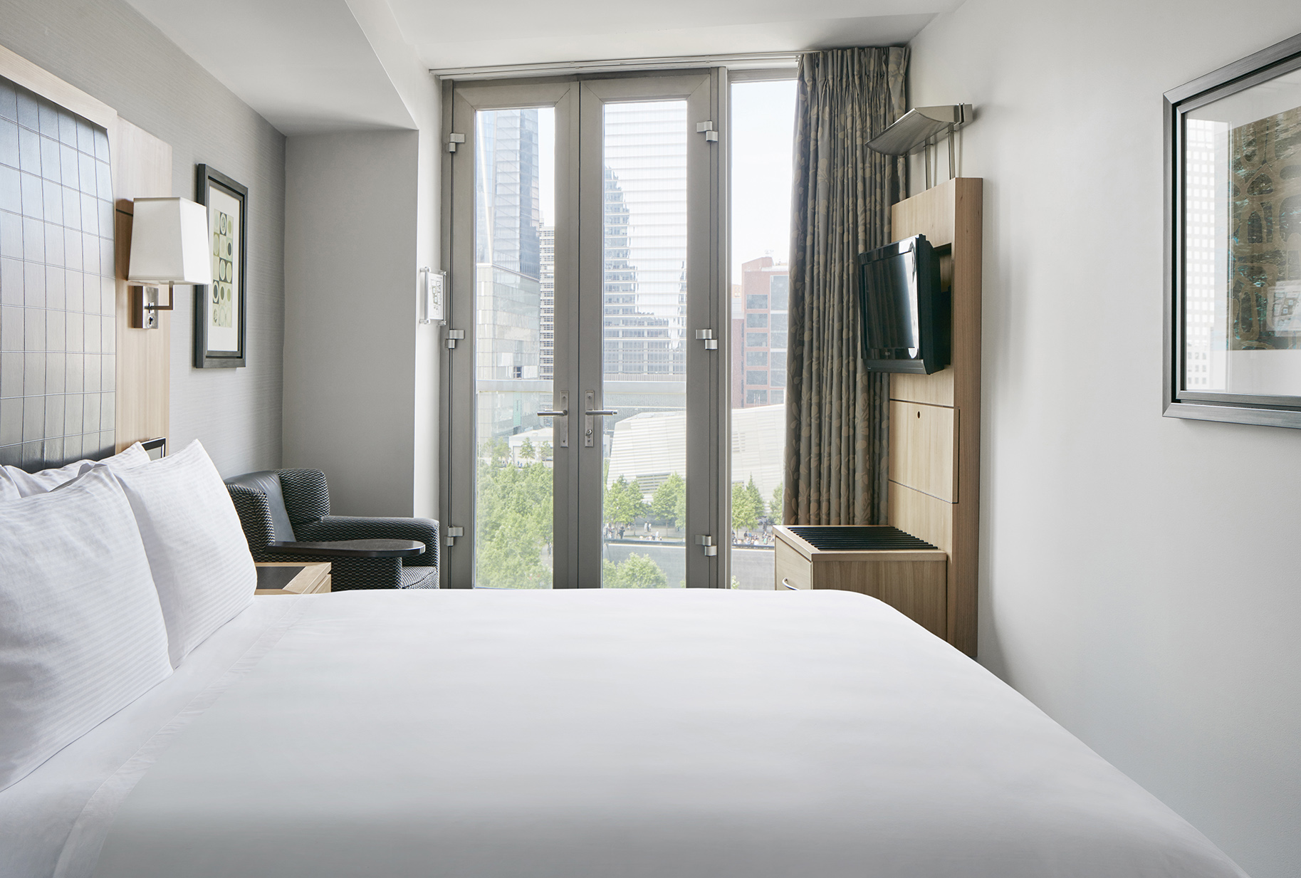 A hotel room with a king-sized bed, a chair, a TV, and a city view.