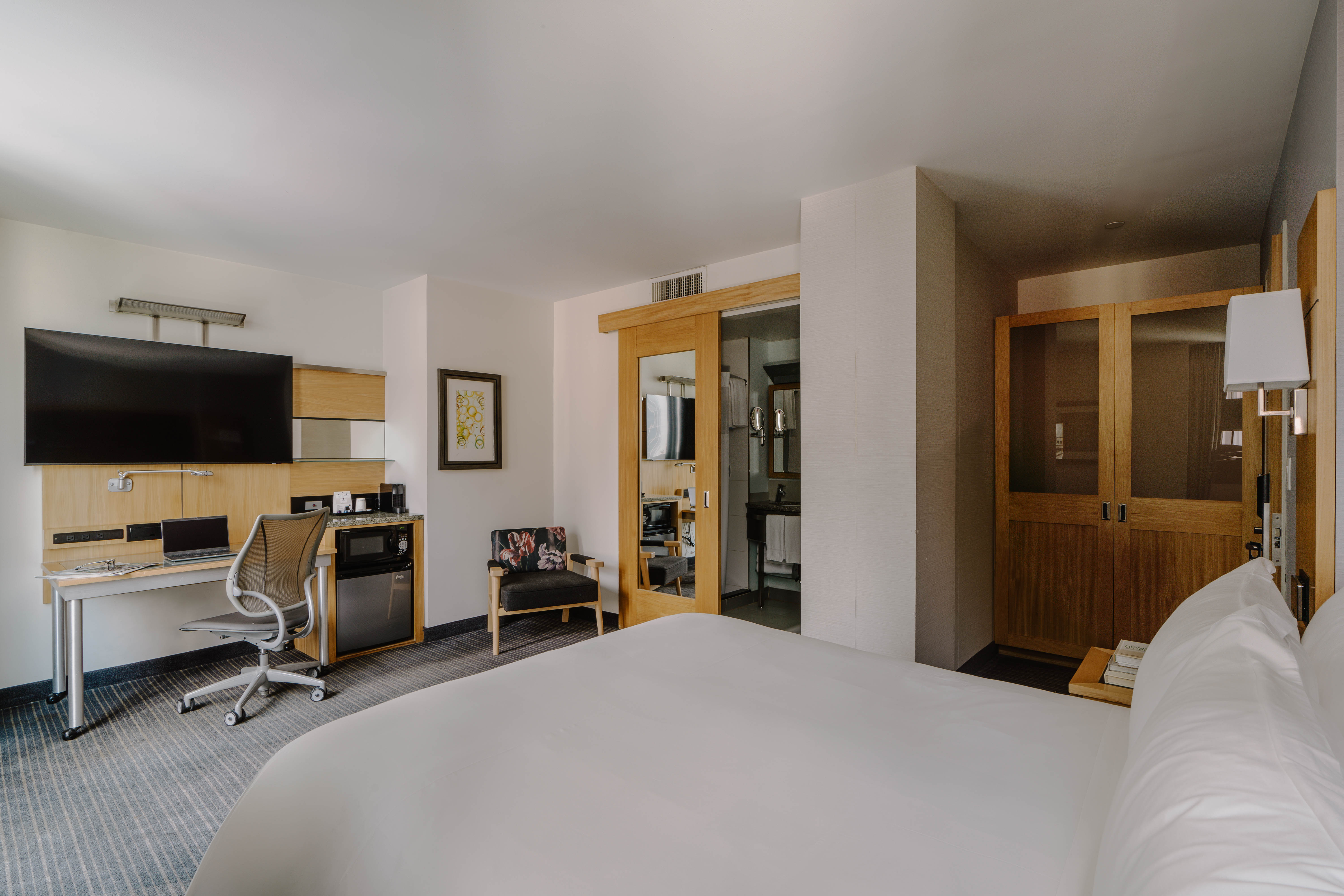 A hotel room with a large bed, desk, TV, mini-fridge, and coffee maker.